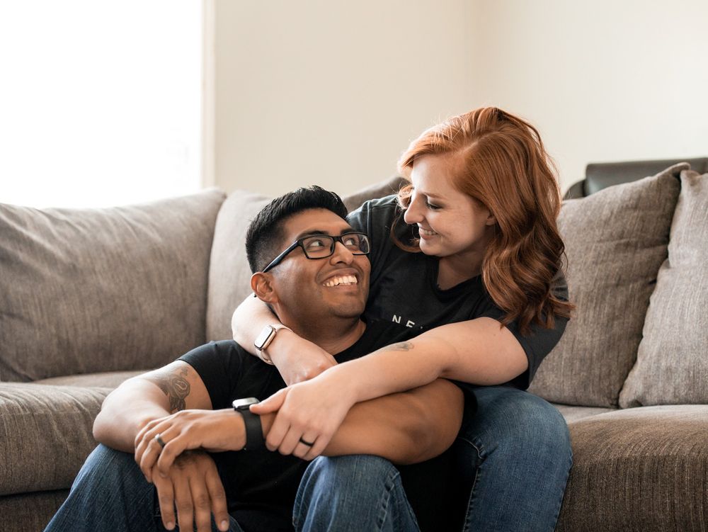 Couple relaxing together on grey couch in living room with natural lighting.