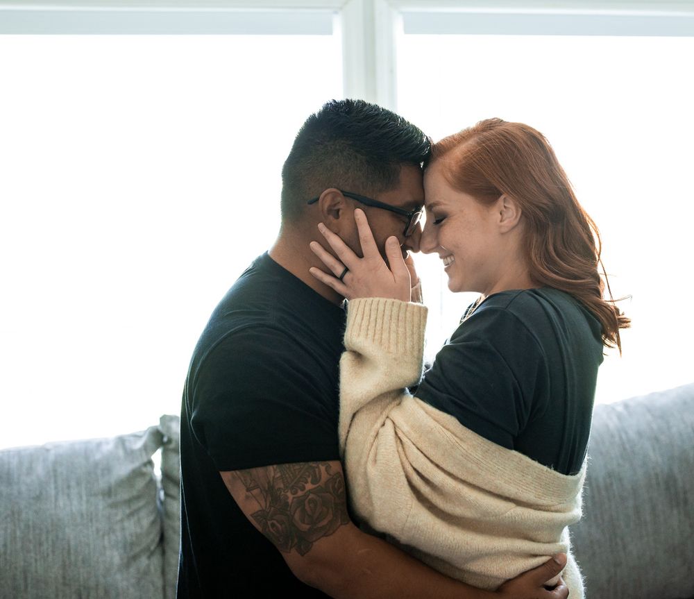 Couple embracing on couch near bright window in casual home setting.