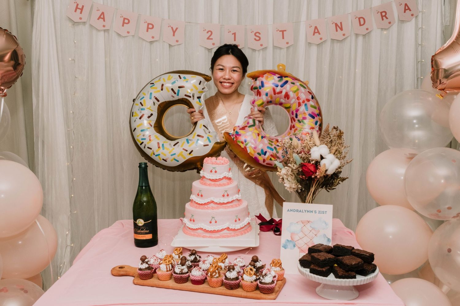 A birthday party display with giant donut decorations, balloons, and a pink tiered cake.