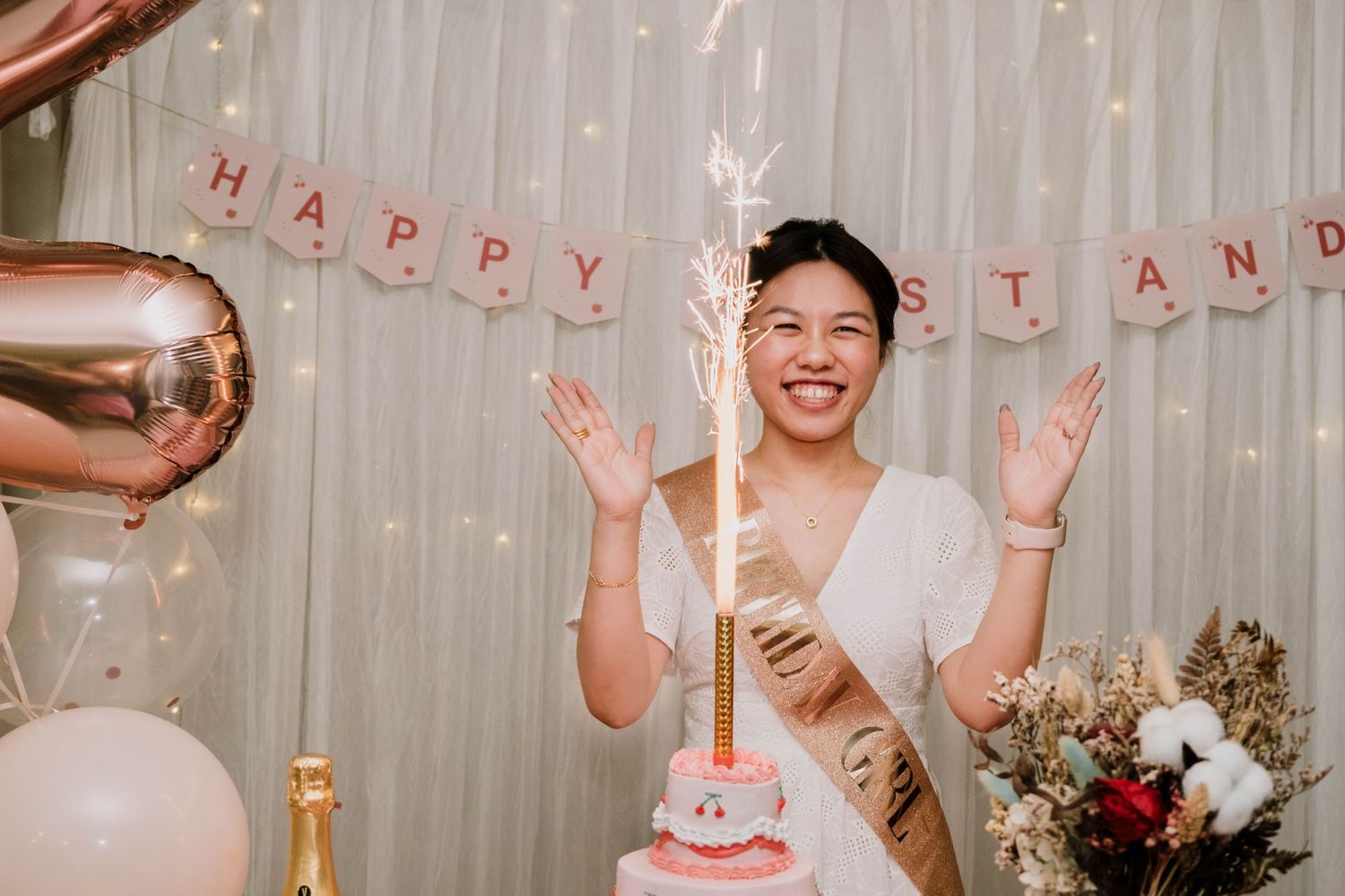 A celebratory scene with rose gold balloons, festive banner, and pink birthday cake.