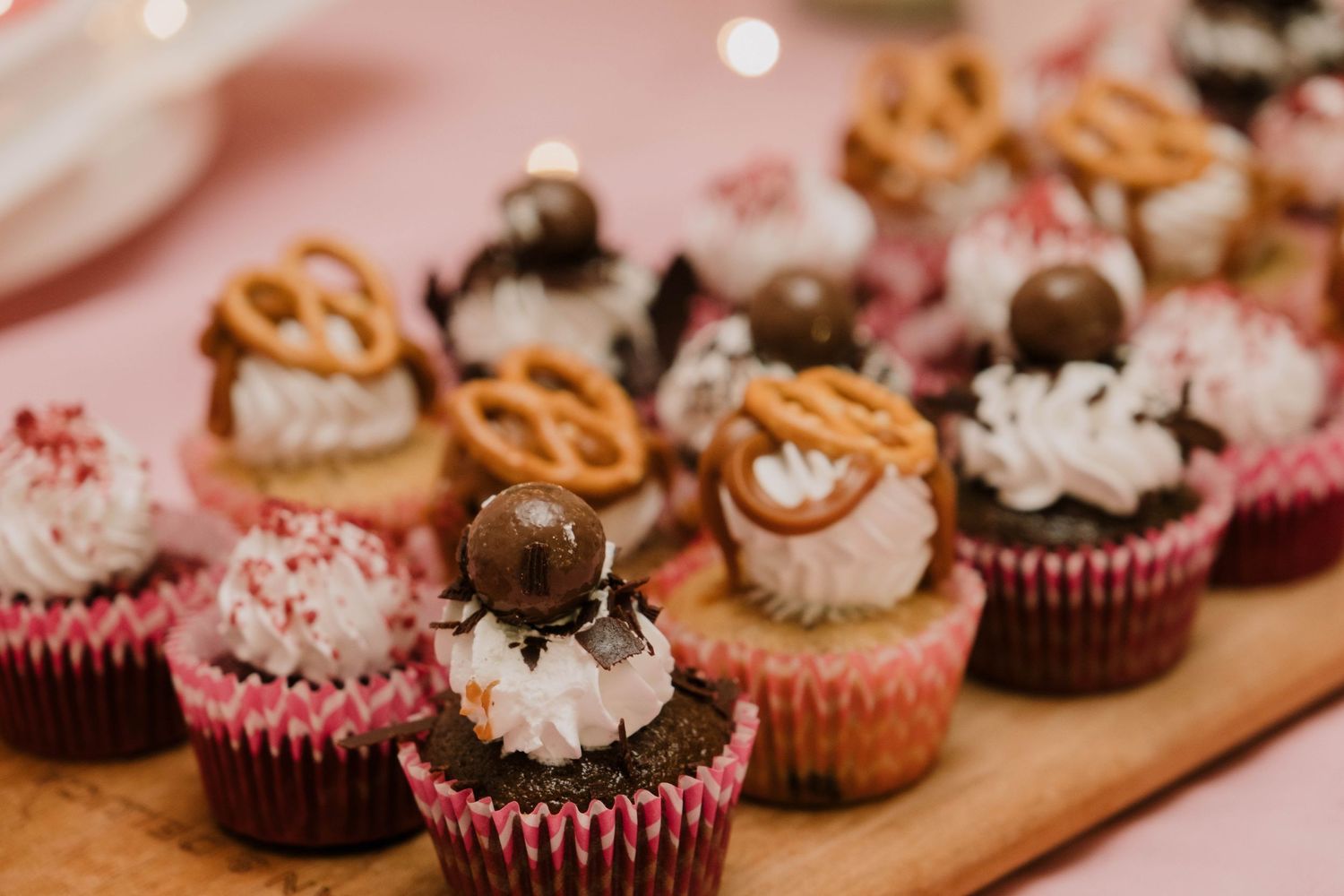 Decorated cupcakes with pretzels and chocolate toppings arranged on a wooden serving board.