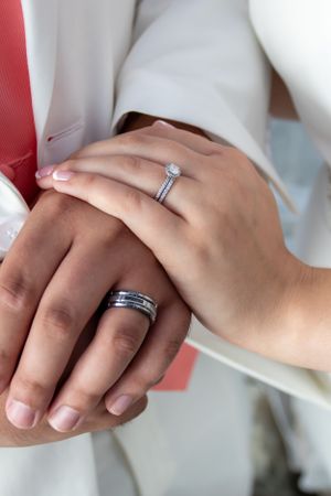 Close-up of hands wearing wedding rings with a solitaire engagement ring and men's band.