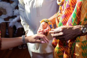Exchange of rings during traditional African wedding ceremony with colorful kente attire.