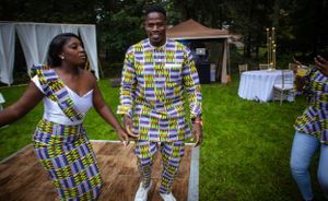 Couple in colorful patterned outfits dancing on grass at an outdoor event.