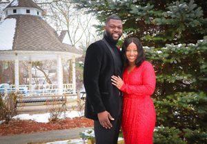 A couple poses in front of a snowy evergreen tree and white gazebo.
