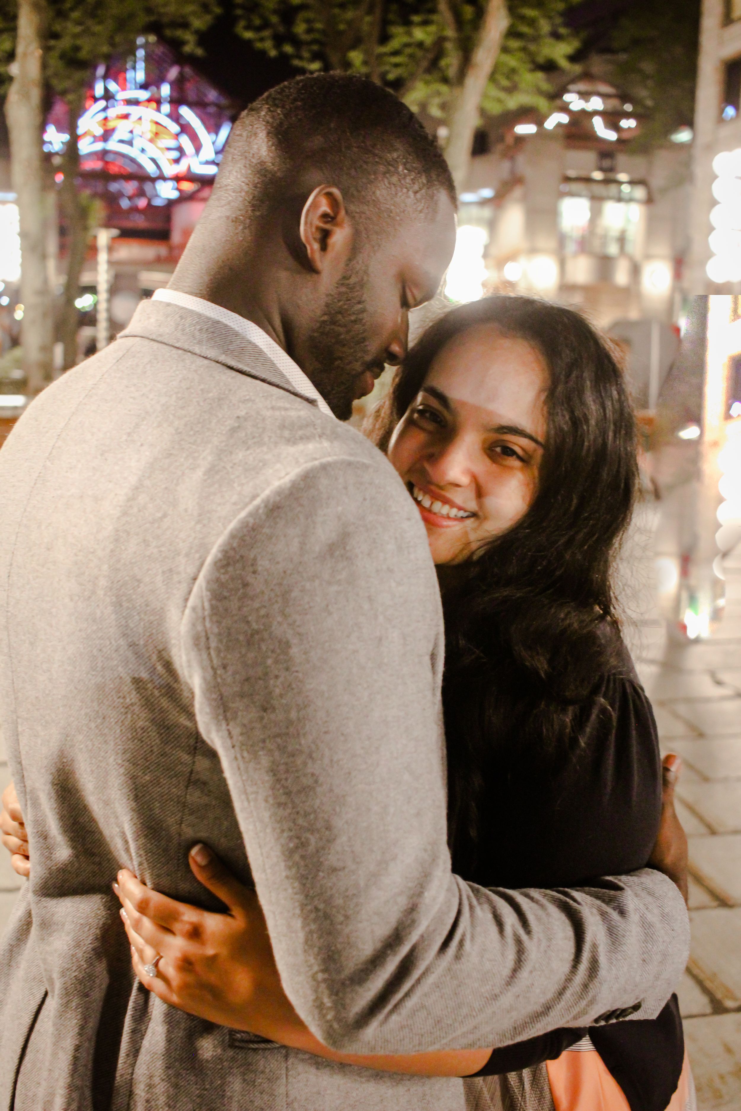 Romantic evening couple embrace under twinkling lights outdoors.
