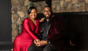 Romantic couple photoshoot against stone wall backdrop in formal red and burgundy attire.