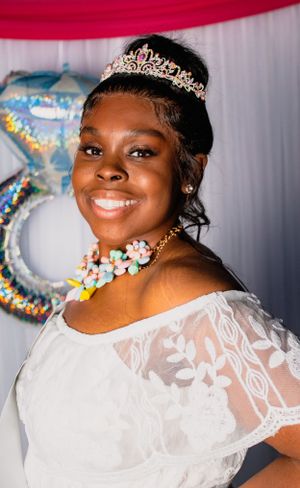 Close-up of woman in white dress wearing tiara and colorful necklace.