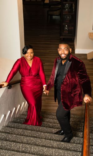 Couple descending stairs in formal red dress and burgundy velvet suit.