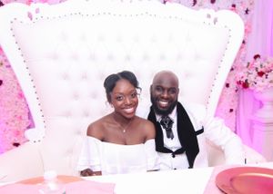Wedding couple seated on white tufted throne chair at reception.