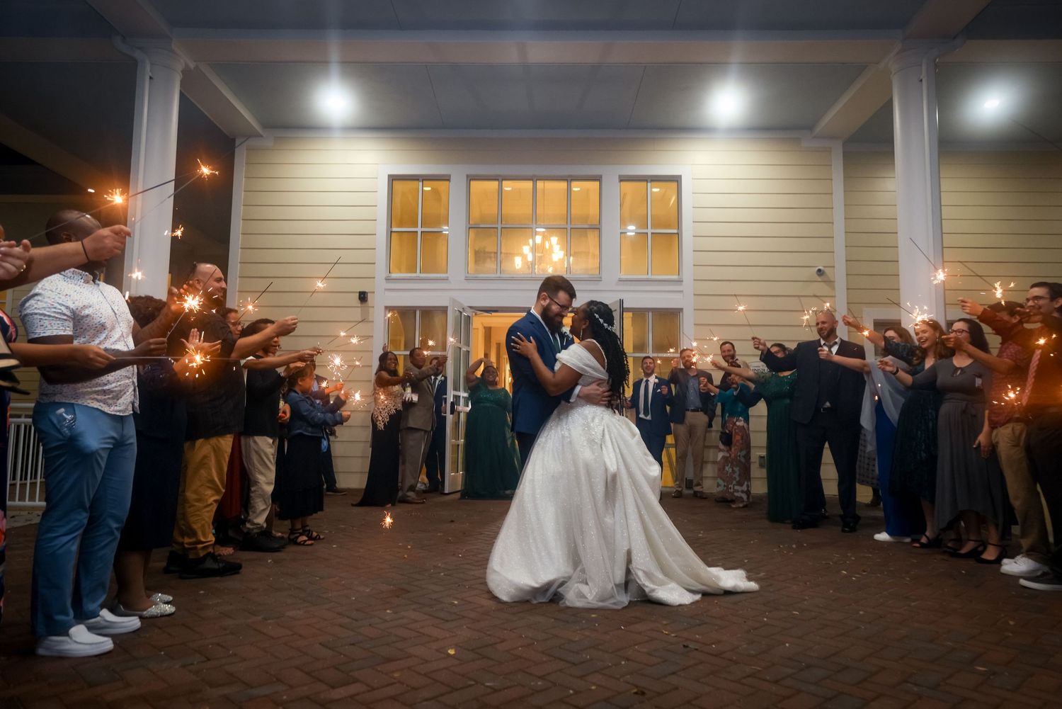 A couple dances at night surrounded by guests holding sparklers creating a magical atmosphere.