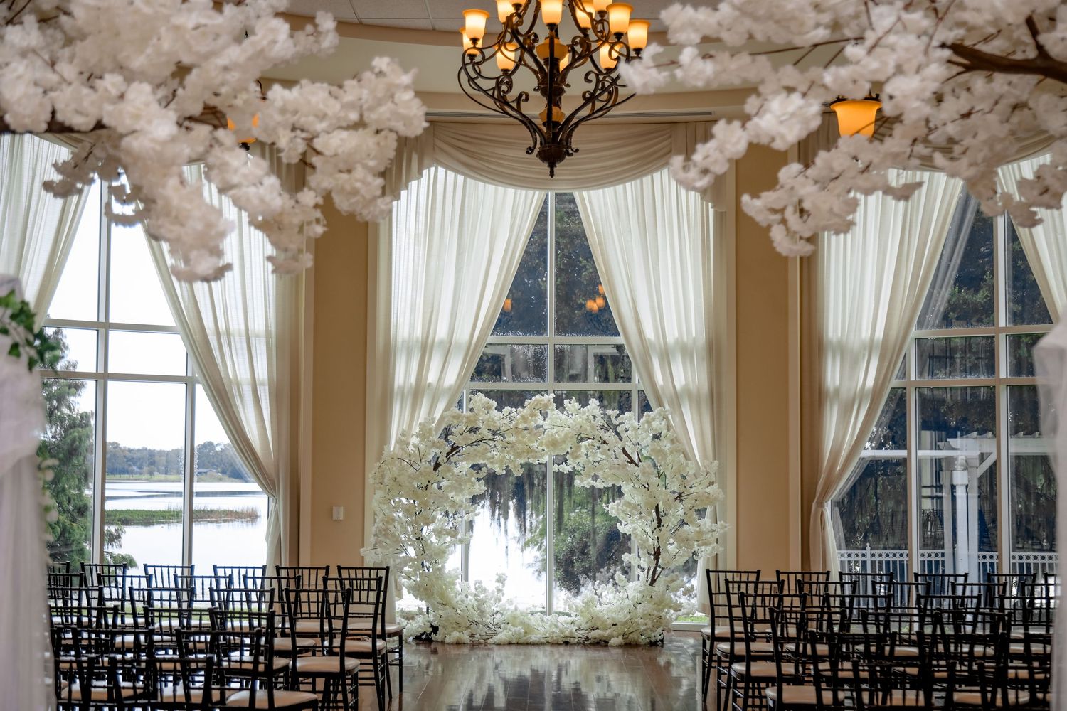Elegant wedding ceremony space with white floral decor, crystal chandelier and draped fabric.