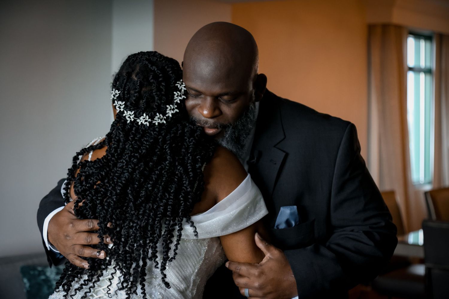 An emotional embrace at a wedding features a black suit-clad figure hugging someone with ornate curly hair.