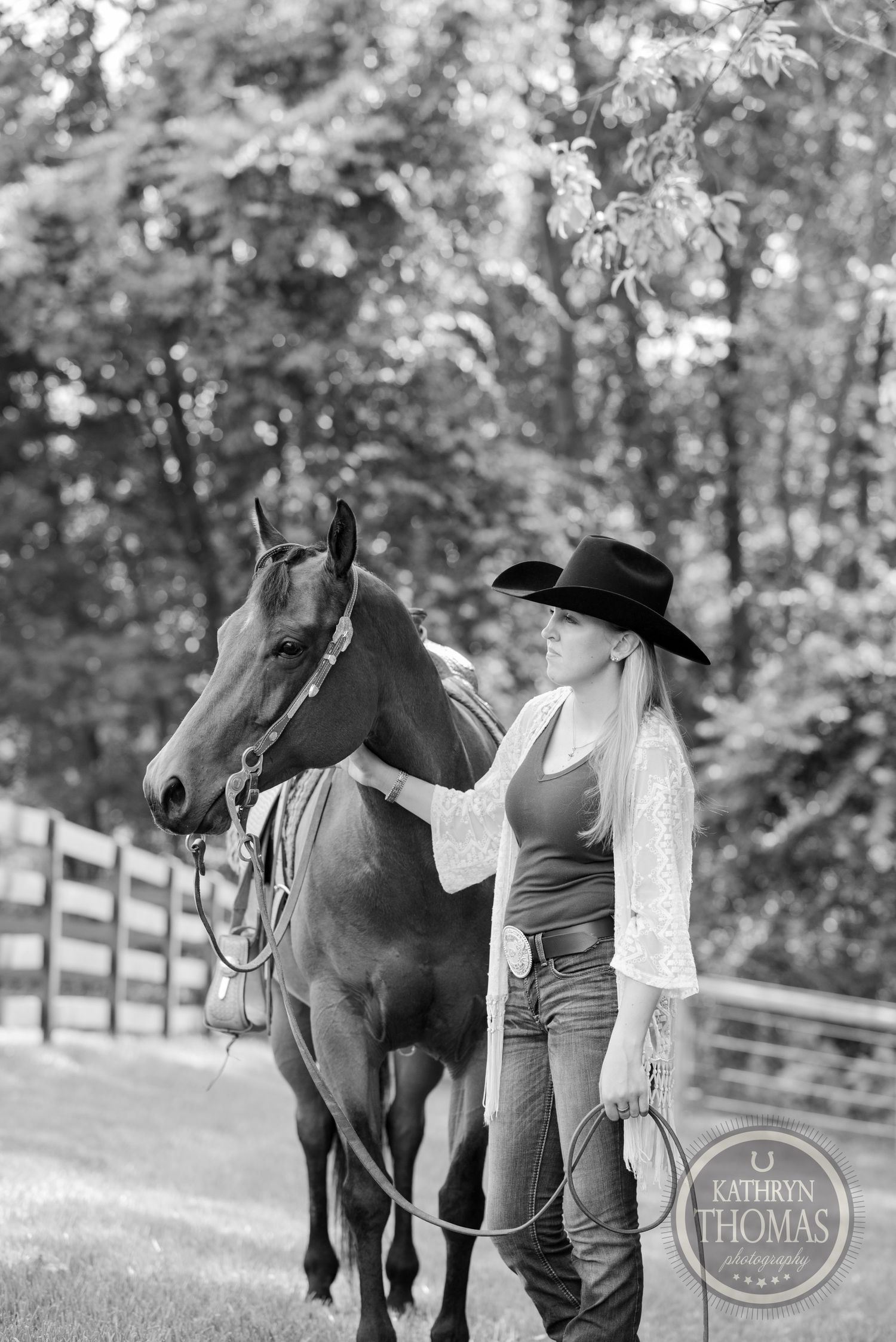 Black and white photo of a horse and someone in western attire by a wooden fence.
