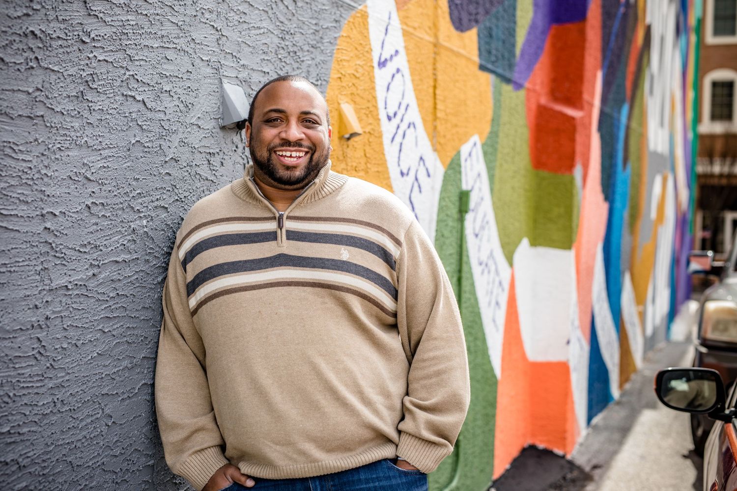 Casual portrait of a person in a striped sweater smiling in front of a colorful mural.