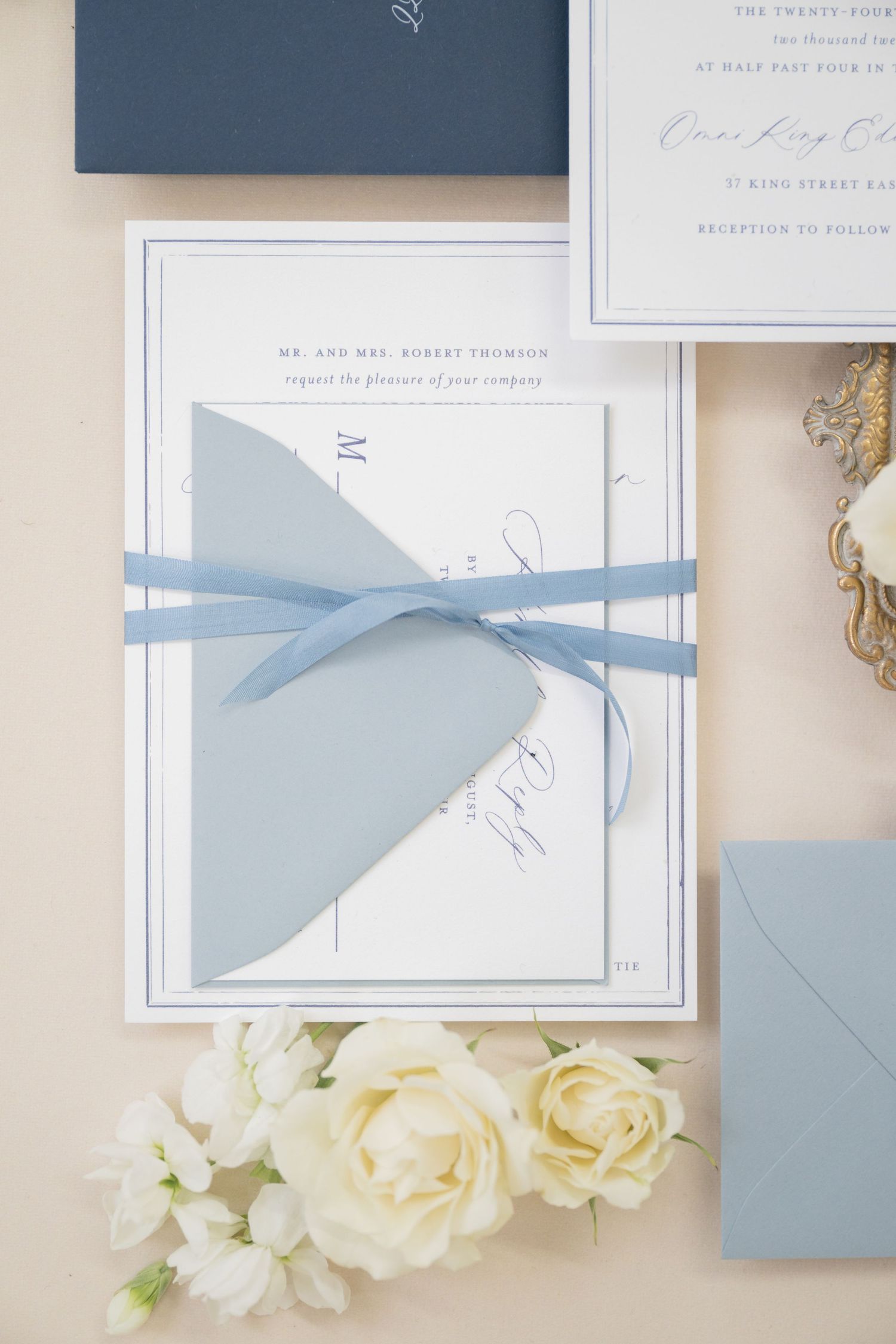 Classic white wedding invitation suite tied with light blue ribbon and decorated with roses.
