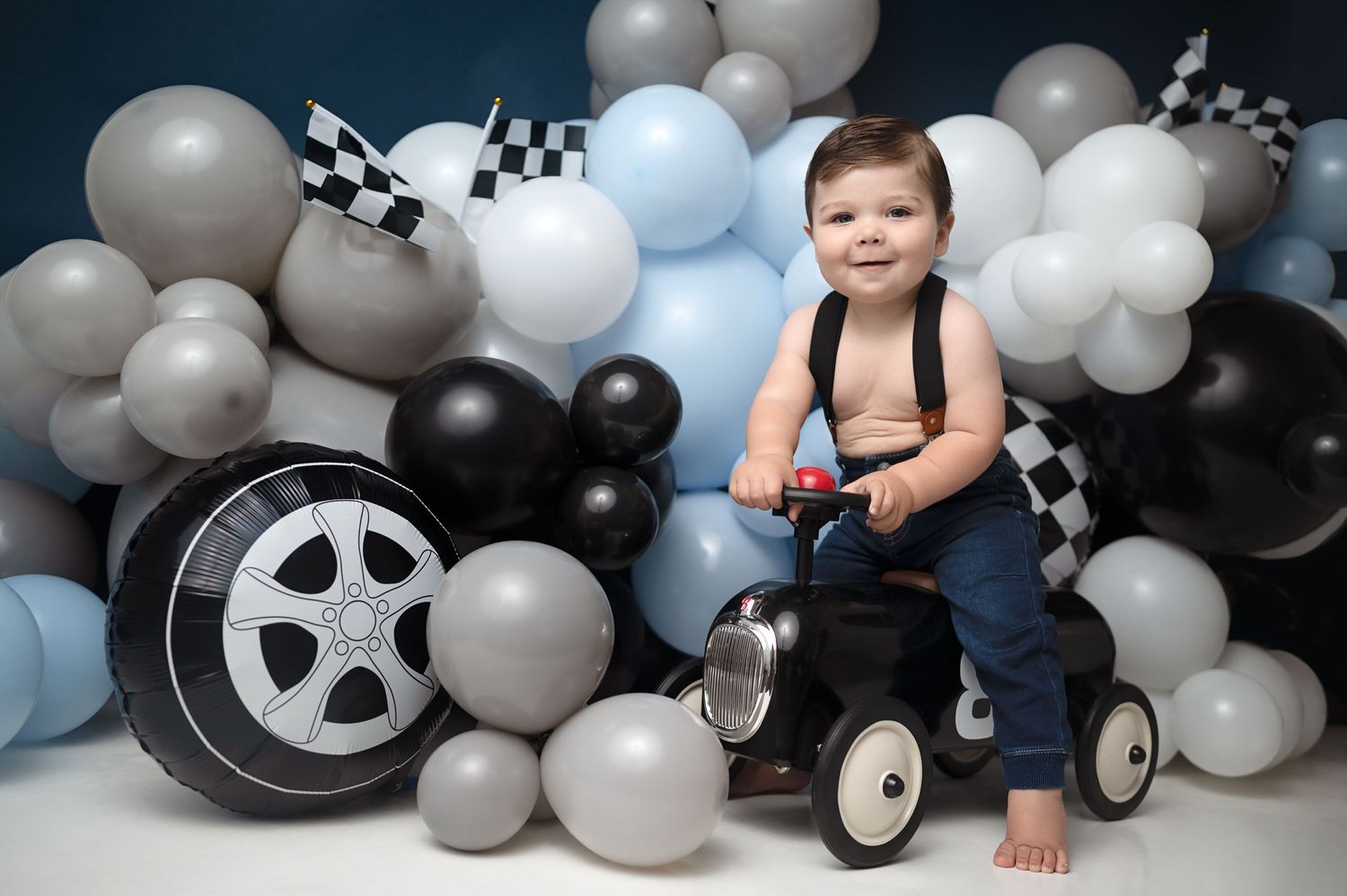 Wide shot of baby with toy car surrounded by festive balloon arrangement.