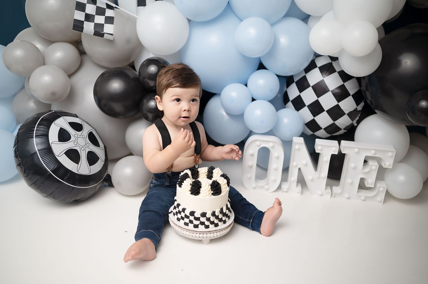 Racing-themed cake smash setup with checkered flags and 'ONE' lettering.