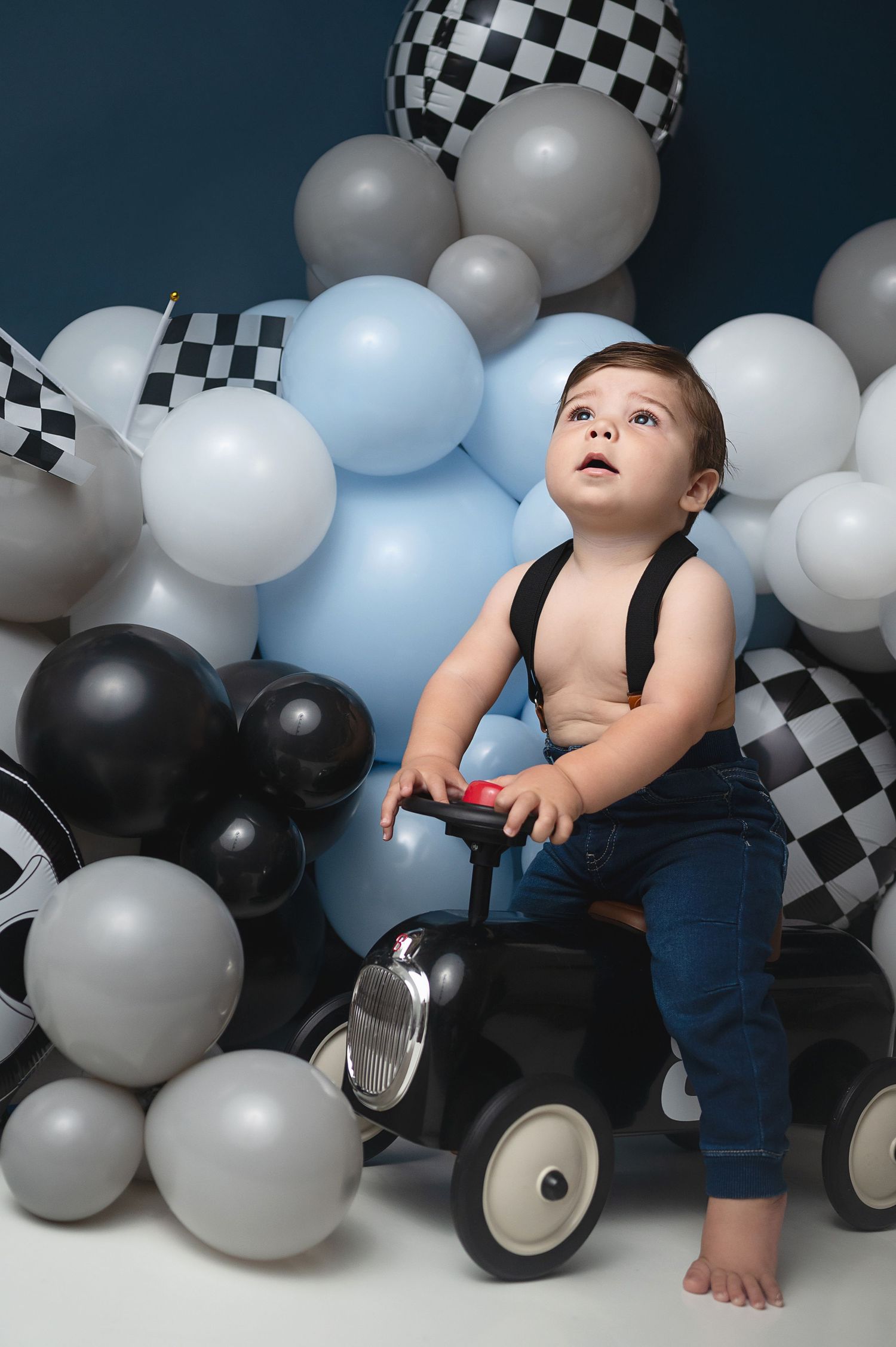 Baby playing with mini car amid blue, black and white balloon display.