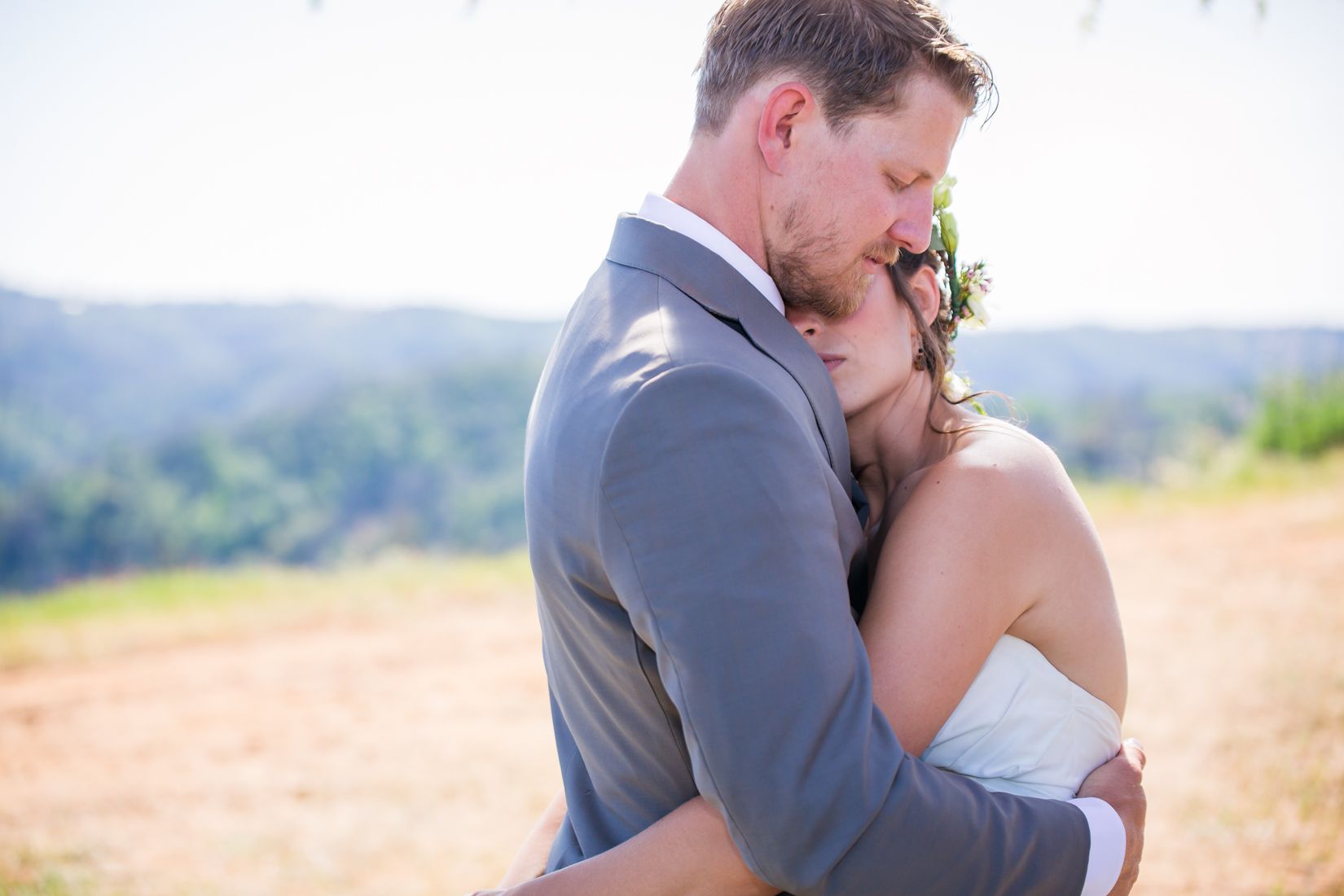 A couple embraces during their outdoor wedding ceremony with mountains in the background.