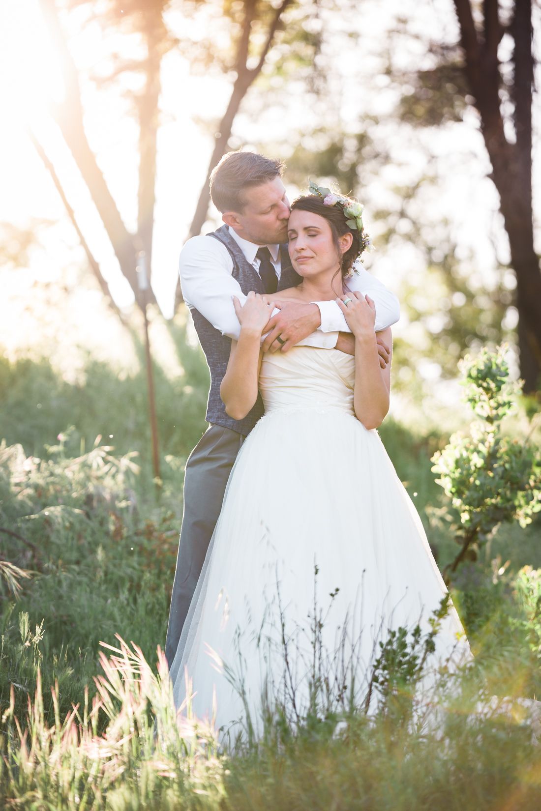 A bride and groom embrace in a sun-lit meadow during golden hour.