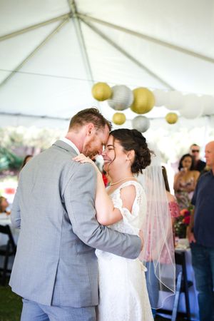 Newlyweds share their first dance under a tent with yellow and white lanterns.