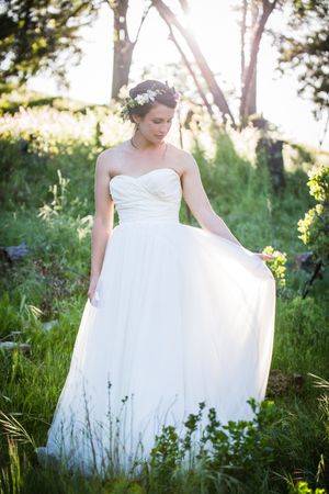A bride in a flowing white dress poses in a sunlit meadow.