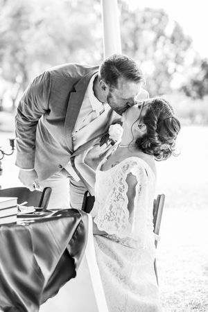 Black and white portrait of a romantic moment between newlyweds at an outdoor wedding table.