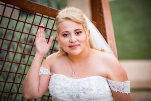 Elegant bride in white dress with blonde hair waves at the camera during outdoor wedding.