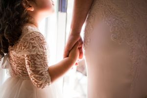Delicate detail shot of lace wedding dress being adjusted in window light.