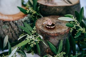Wedding rings displayed on rustic wood slice with green foliage decor.