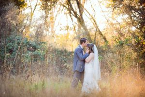 Newlyweds embracing in tall grass during golden hour.