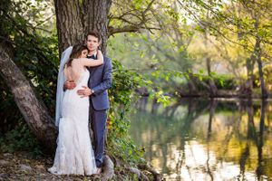 Bride and groom embrace by tranquil pond in autumn setting.