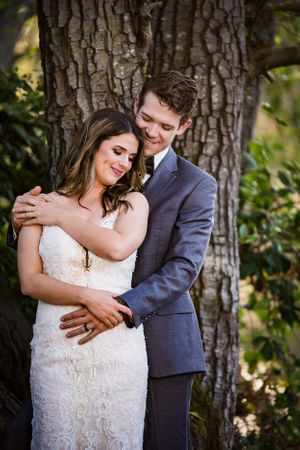 Wedding couple poses intimately against large tree trunk.