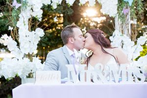 Newlyweds share romantic kiss behind Mr & Mrs sign with white orchids and sunset backdrop.