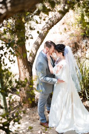 Couple shares tender moment under tree during wedding photoshoot.