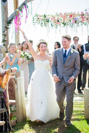 Joyful celebration under flower-adorned canopy during outdoor wedding ceremony.