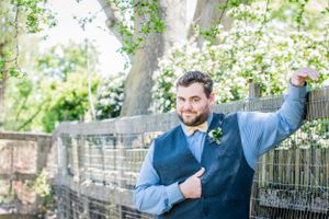 Man in blue vest poses playfully against ornate garden fence.