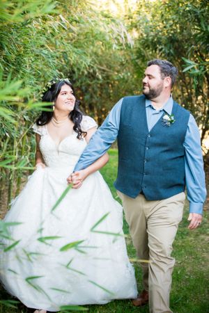 Newlyweds walking hand in hand through bamboo garden path.