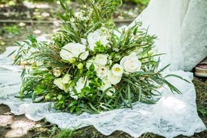 Elegant white and green wedding bouquet with roses and eucalyptus rests on lace fabric.