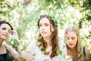 Three women in nature with sun-dappled background and floral crowns.