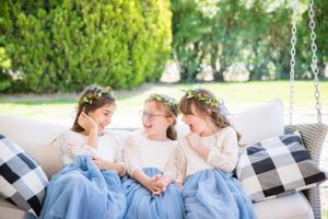 Three flower girls in matching blue dresses laughing together on a porch swing.