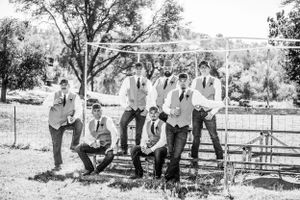 Black and white photo of groomsmen posing casually against a rustic fence.