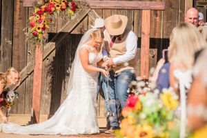 Rustic barn wedding ceremony with bride and groom surrounded by colorful floral decorations.