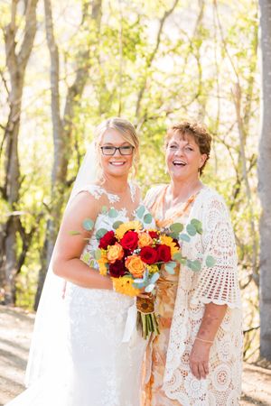 A bride holding a vibrant fall-colored bouquet poses in a sunny wooded setting.