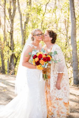 Two people share a tender moment in white lace dresses with a colorful autumn bouquet.