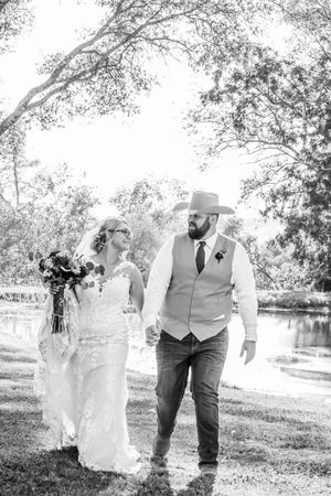 Black and white wedding portrait of couple walking together in a scenic outdoor setting.