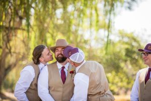 Groomsmen in tan vests and cowboy hats having fun during outdoor wedding photos.