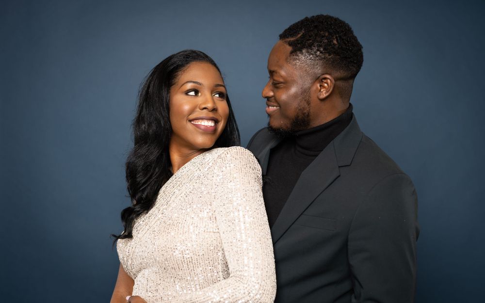 A couple shares a joyful moment in formal attire against a dark background.