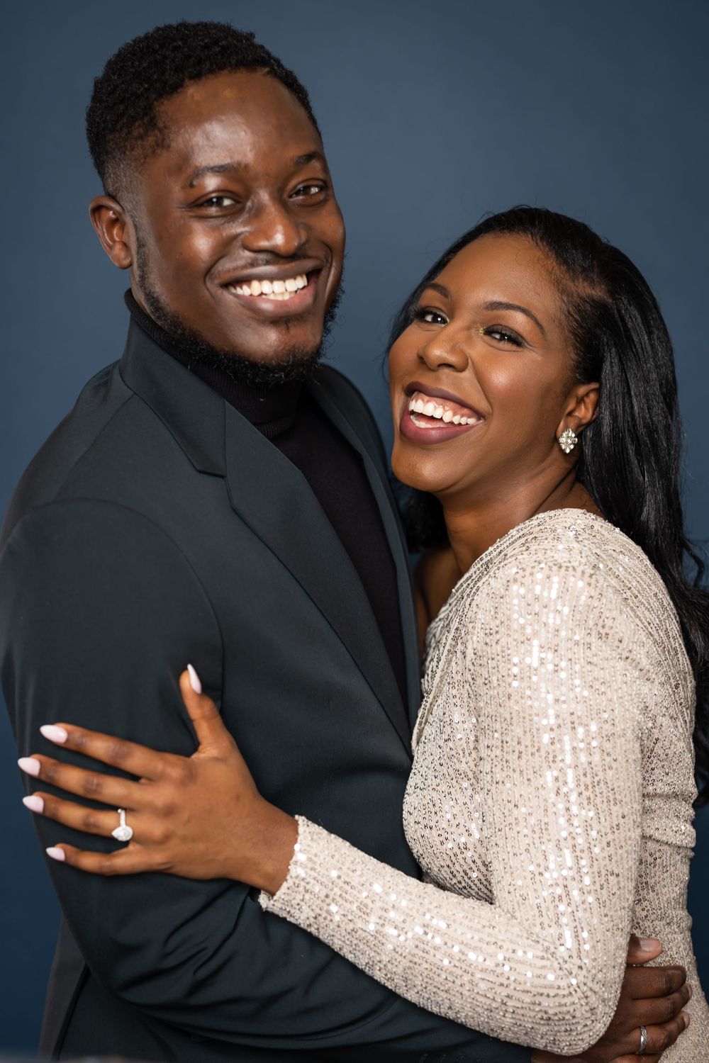 A couple laughs together during their engagement photo session against a dark background.
